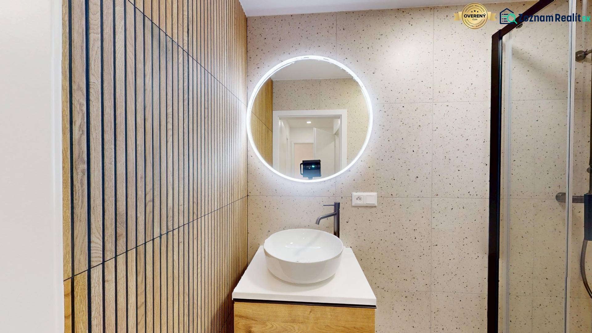 A hallway from a 4-room apartment with a sink, a mirror, and a wall with a wooden decor.