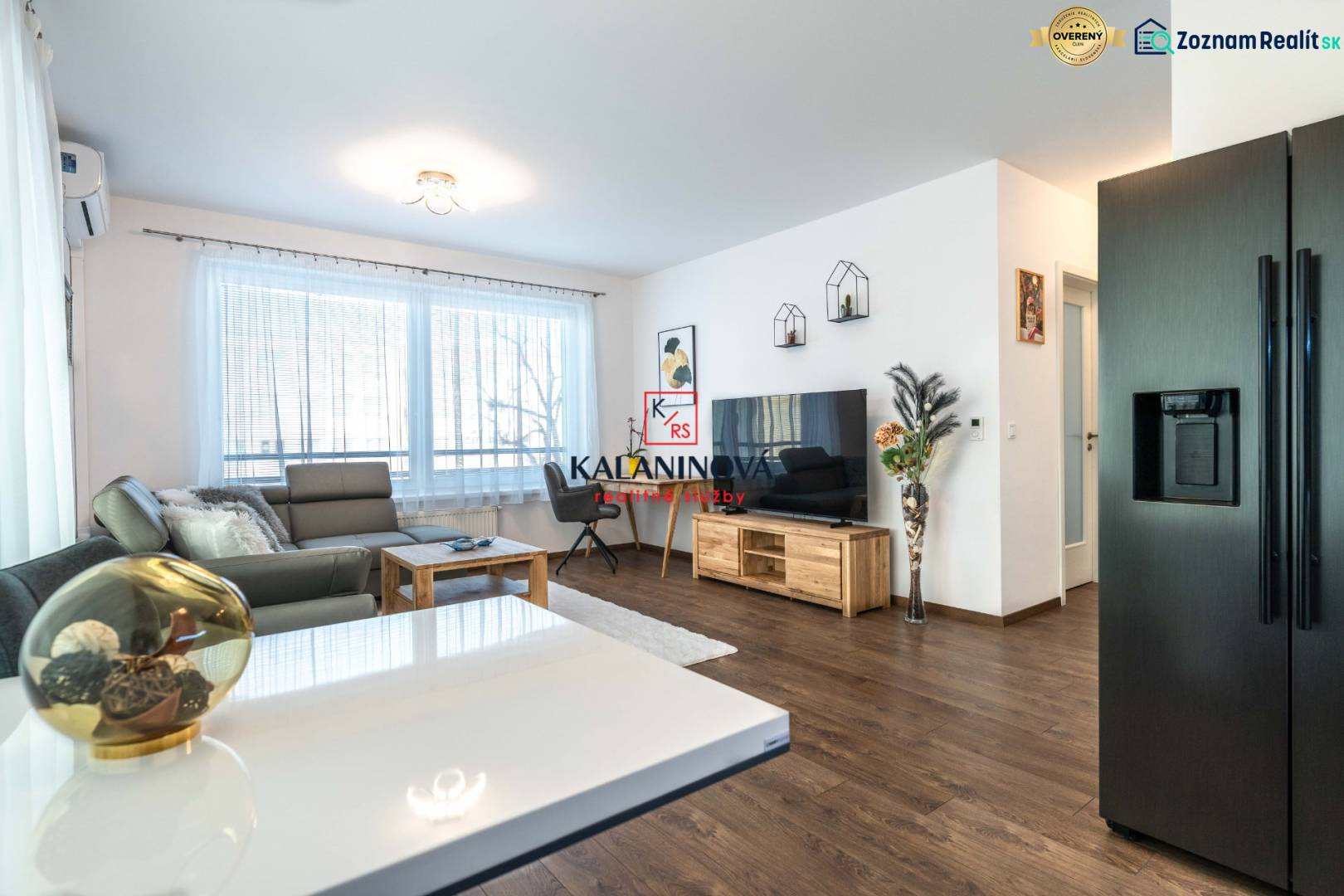 Living room in a two-room apartment with a wood-patterned floor and large windows.