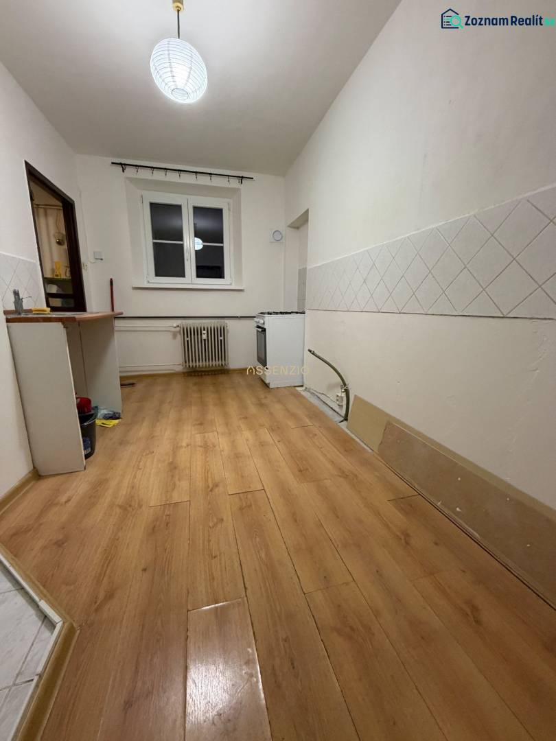 Kitchen in a studio apartment, wooden decor flooring, white tiles on the walls.