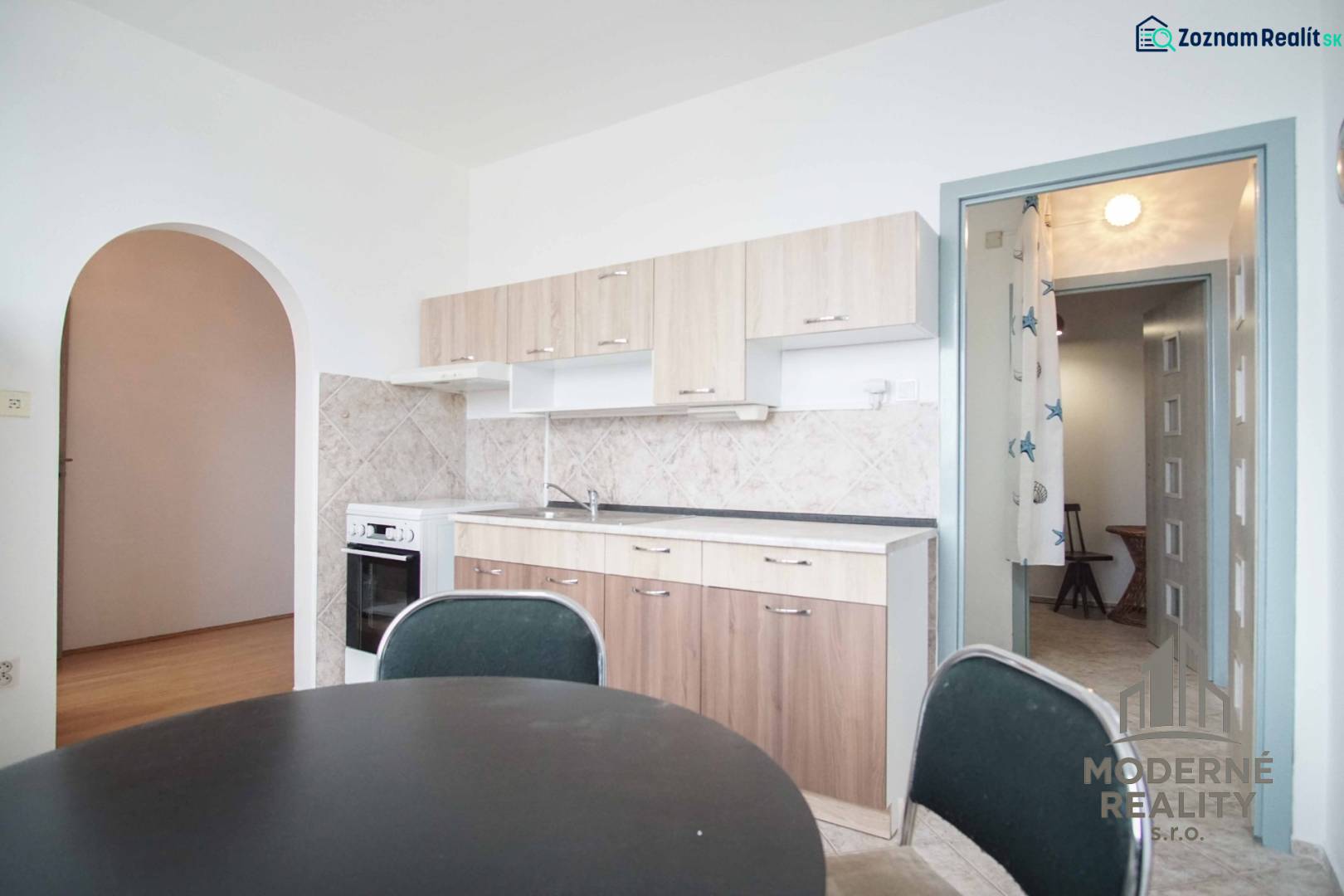 A kitchen in a 3-room apartment with a wooden decor floor and an arched entrance.