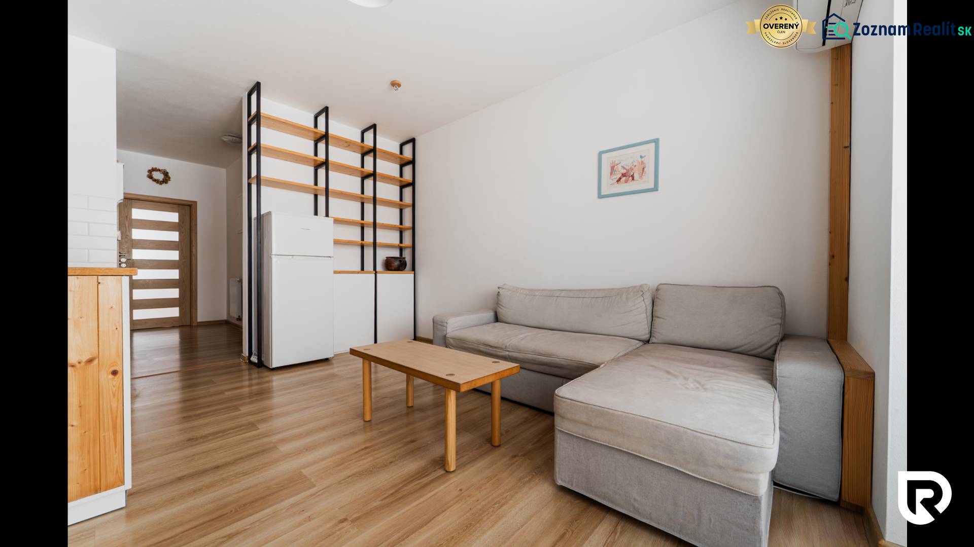 Living room in a two-room apartment with a sofa, table, and wooden decor flooring.