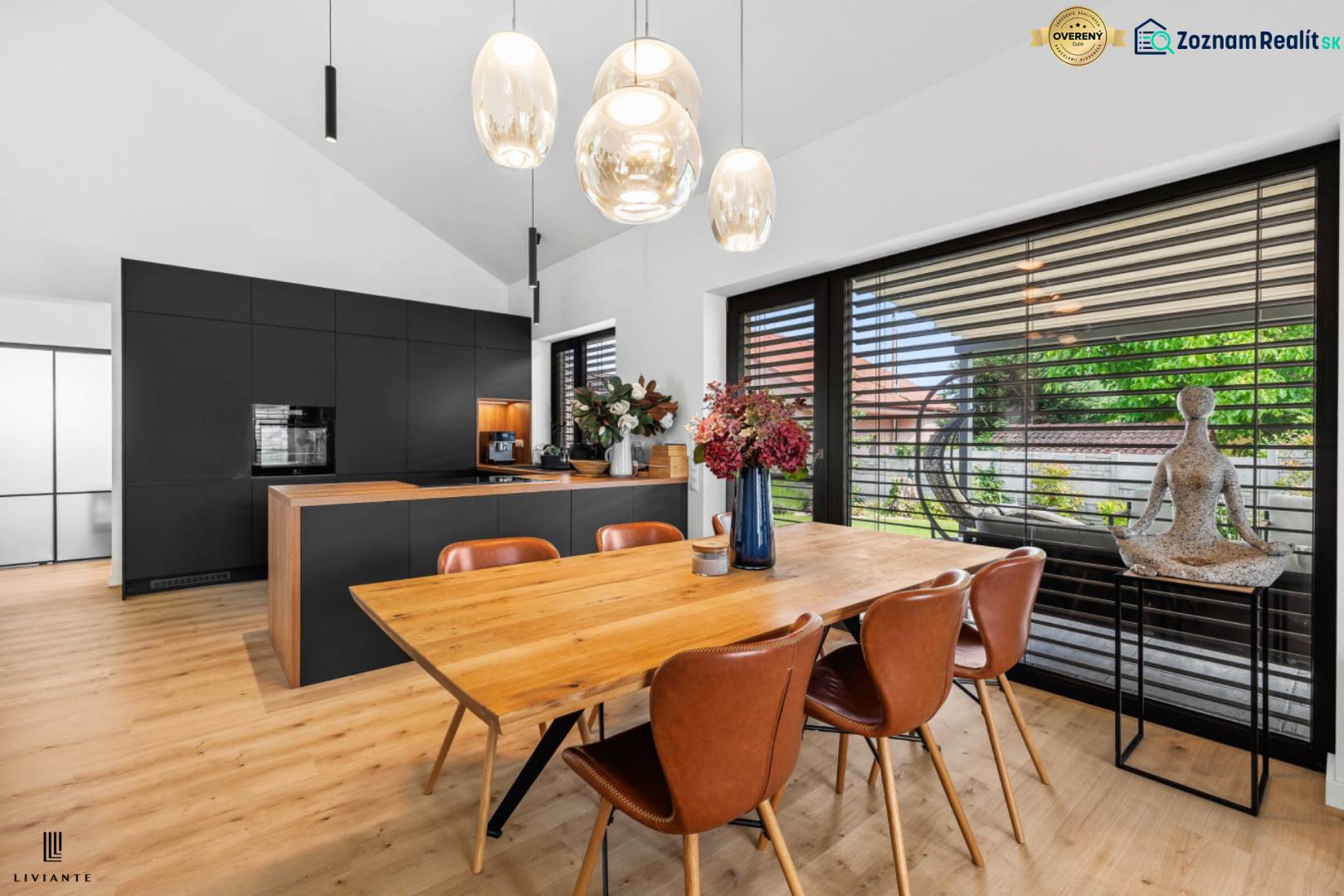 Dining room with a wooden table and black kitchen unit in a family house.