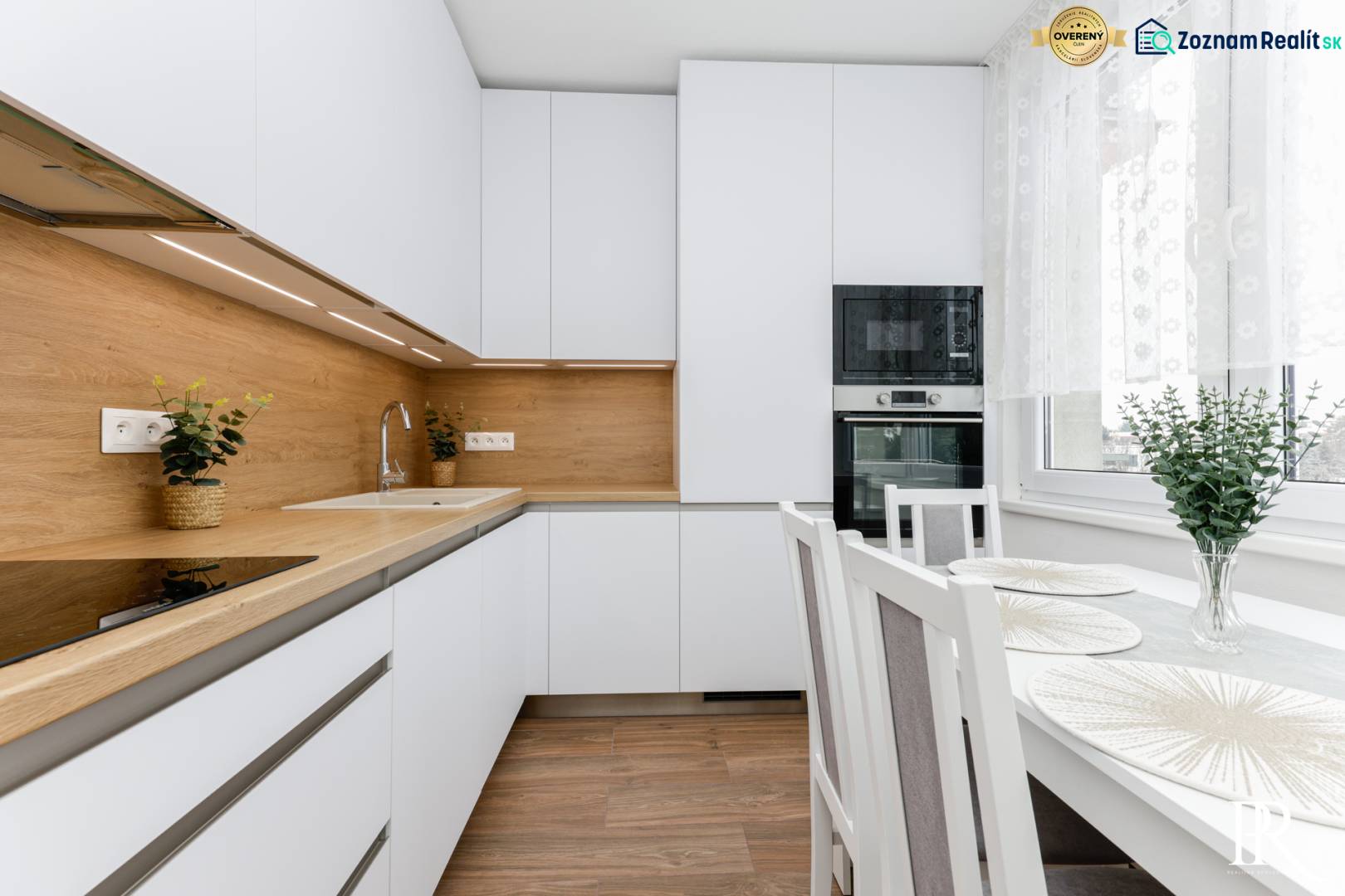 A kitchen with white cabinets, wooden decor, and a dining table in a two-room apartment.