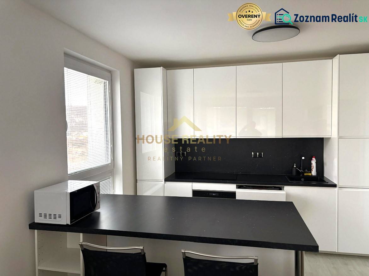 A kitchen in a 2-room apartment with white cabinets and a black countertop.