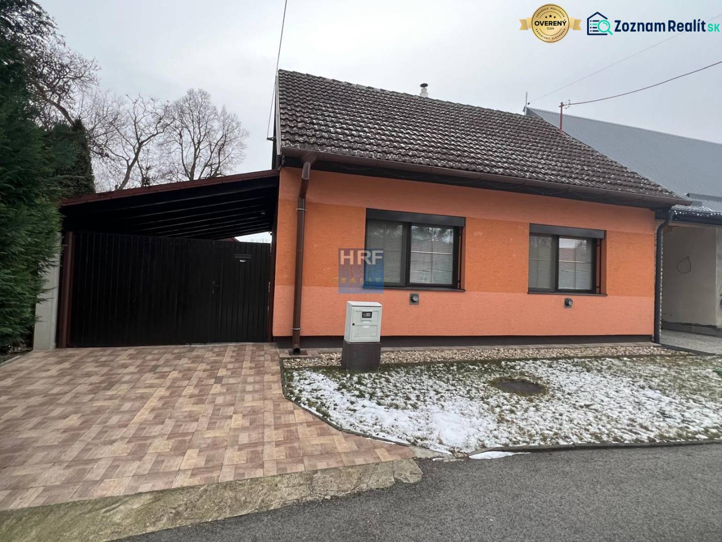 A family house in Dubovce with an orange facade, a garage, and a garden with a light dusting of snow.