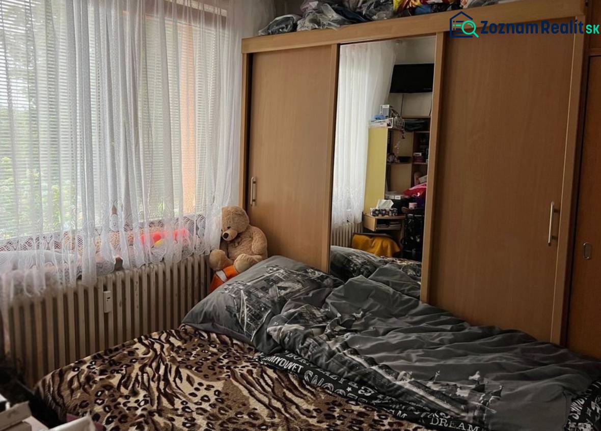 Bedroom in a studio apartment with a bed, a wardrobe with a mirror, and a plush teddy bear.