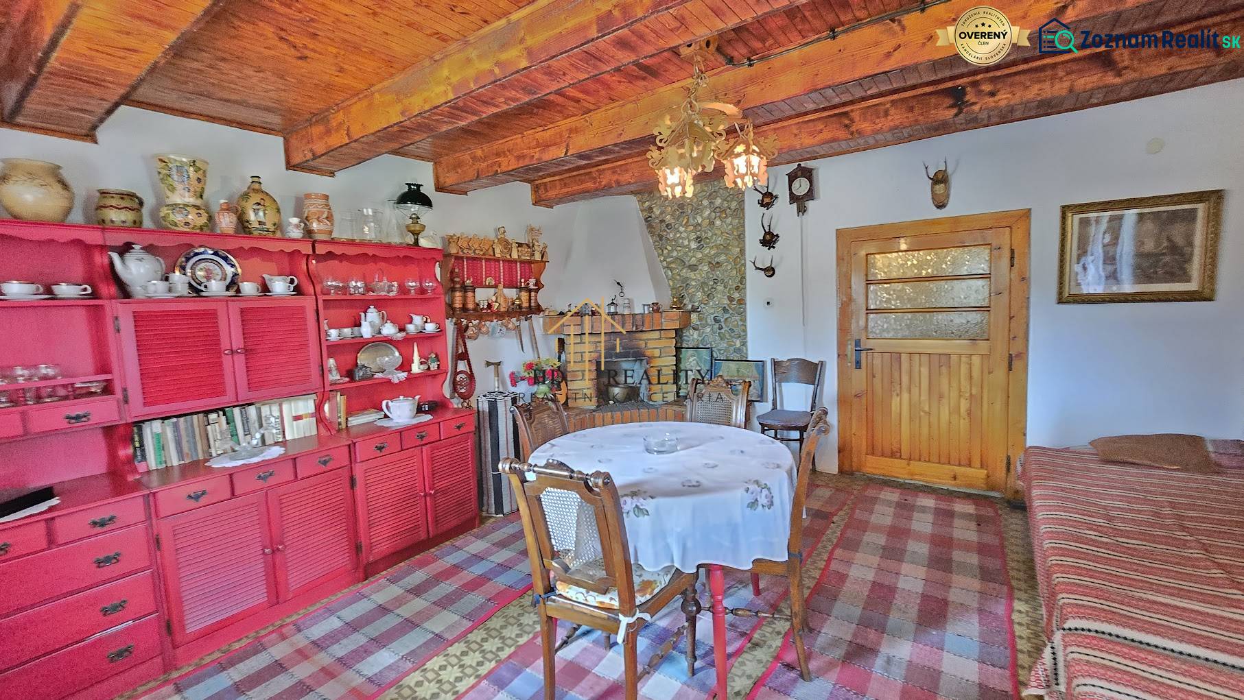 The interior of a family house with a wooden ceiling, a red cabinet, and a dining table.