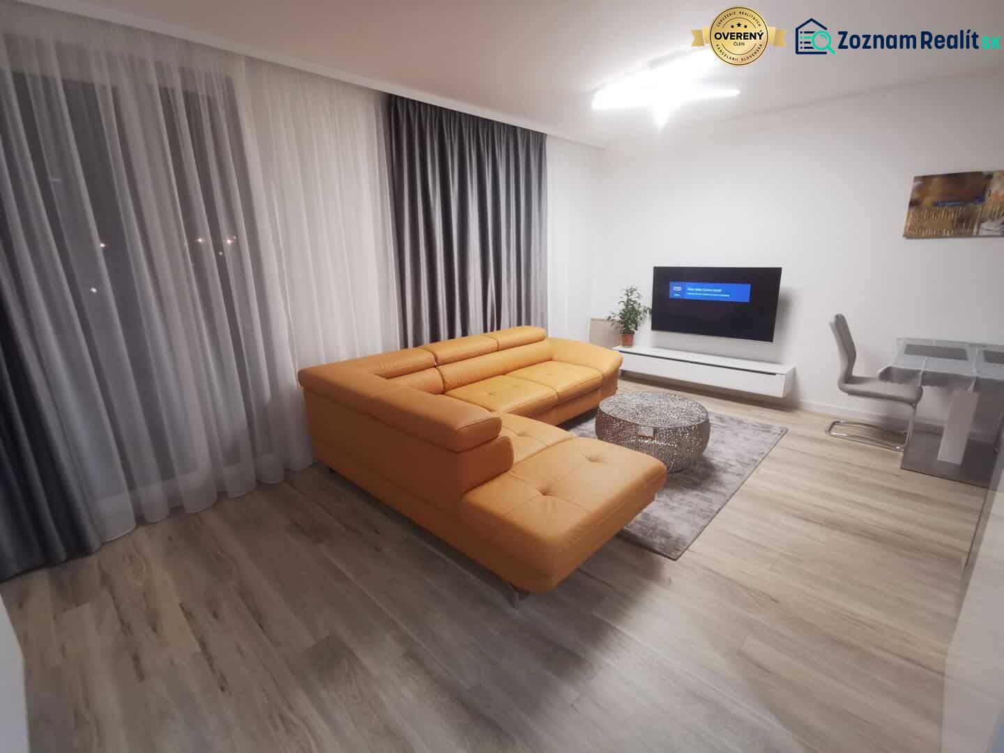 Living room in a two-room apartment with an orange sofa and a wooden decor floor.