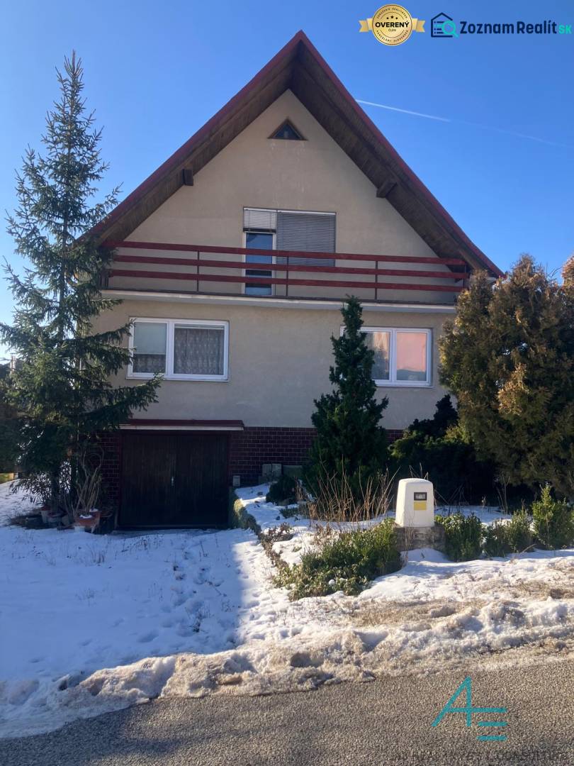 A family house on the street in Rudník, a snowy garden with conifers in the foreground.