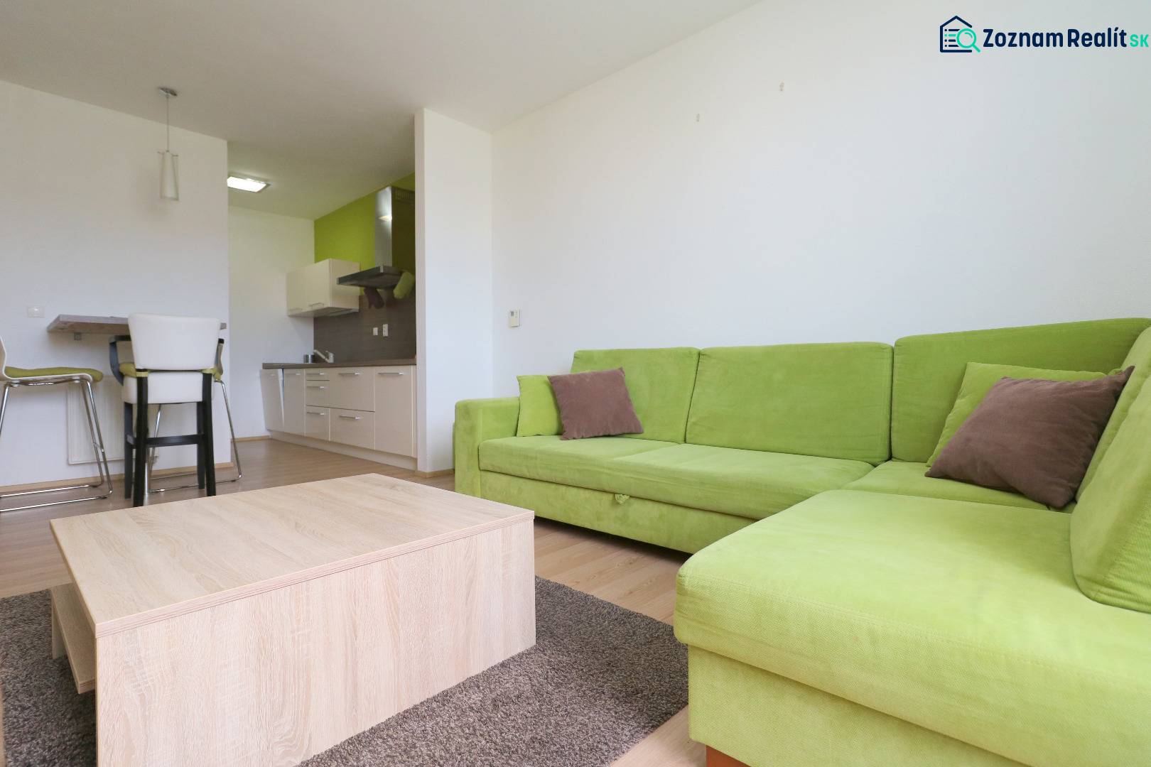 Living room in a two-room apartment with a wooden decor floor and a green sofa.