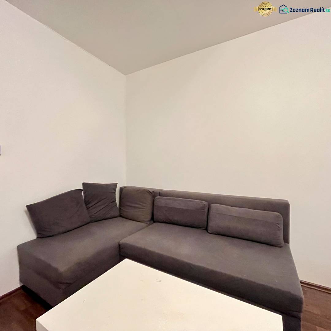 Gray corner sofa with cushions next to a white table in a studio apartment.