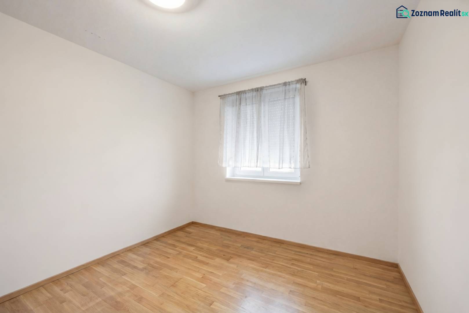 A room with a window, a white wall, and a wooden decor floor in a family house.