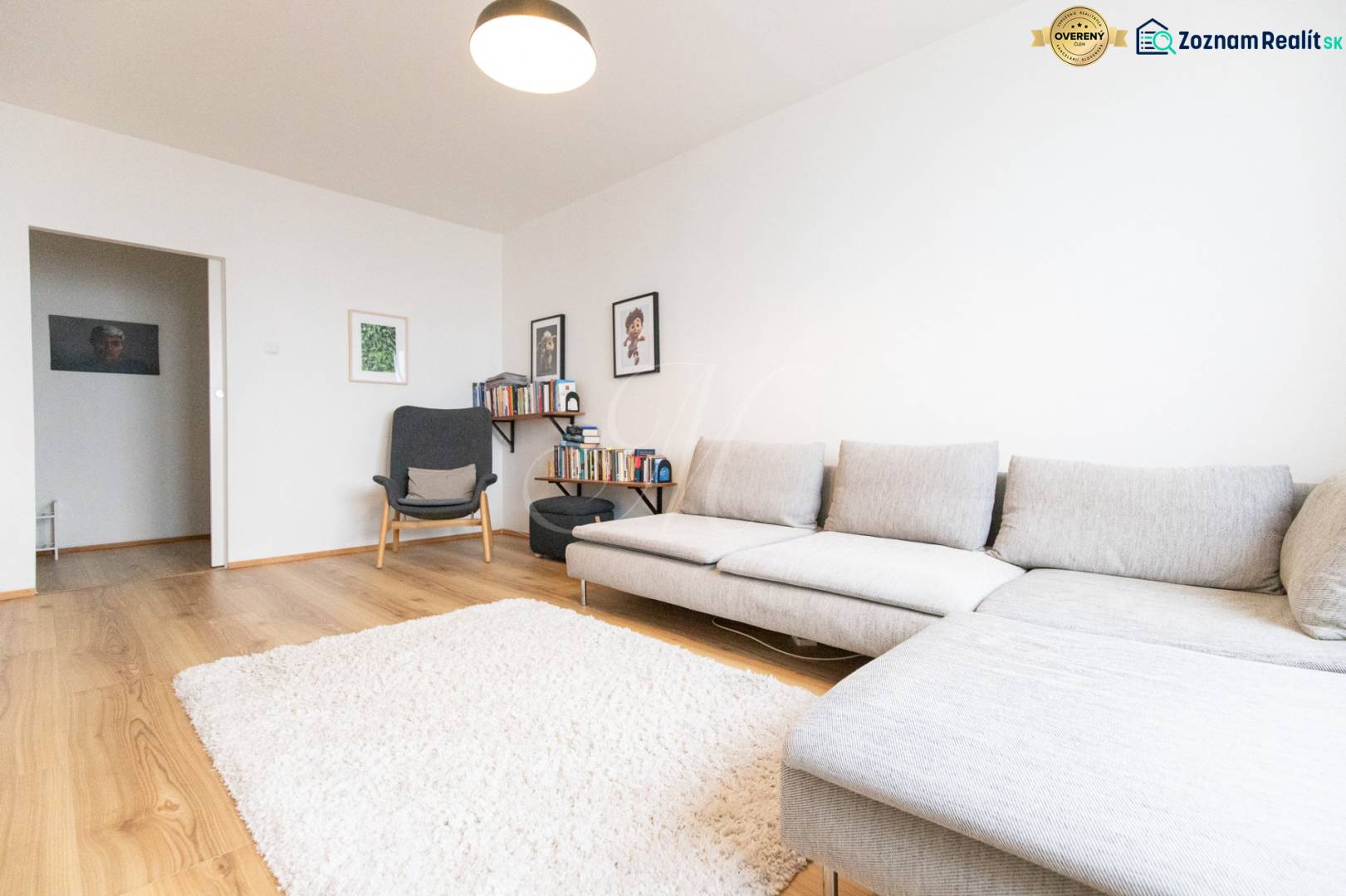 Living room in a three-room apartment with a wooden decor floor, gray sofa, and books.