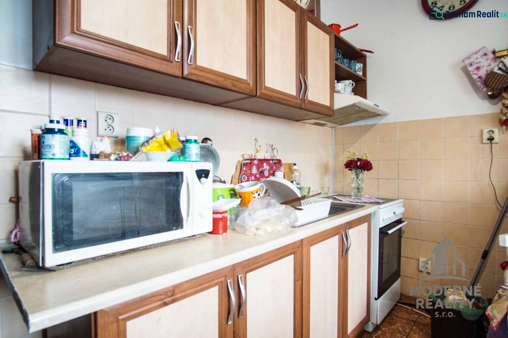 A kitchen with a microwave, a gas stove, and wooden cabinets in a two-room apartment.