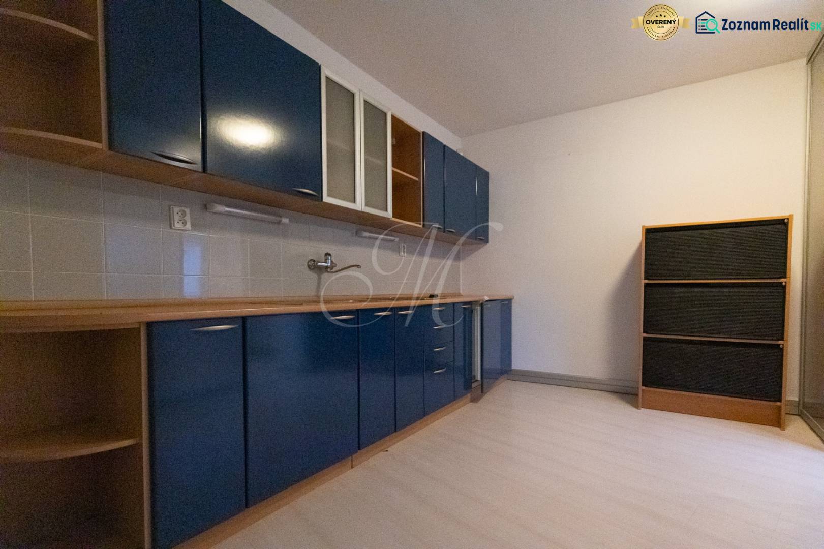 A kitchen in a 4-room apartment with cabinets, white tiles, and a wooden decor floor.