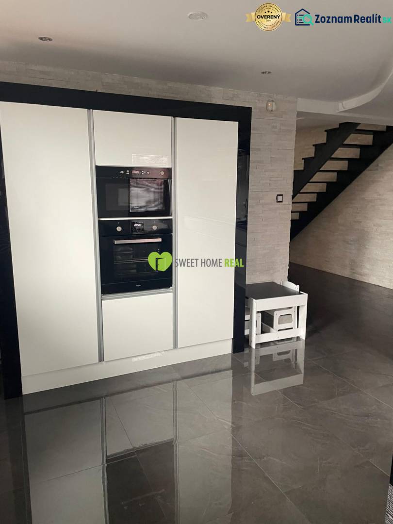 A kitchen in a family house with a glossy black floor and white appliances.