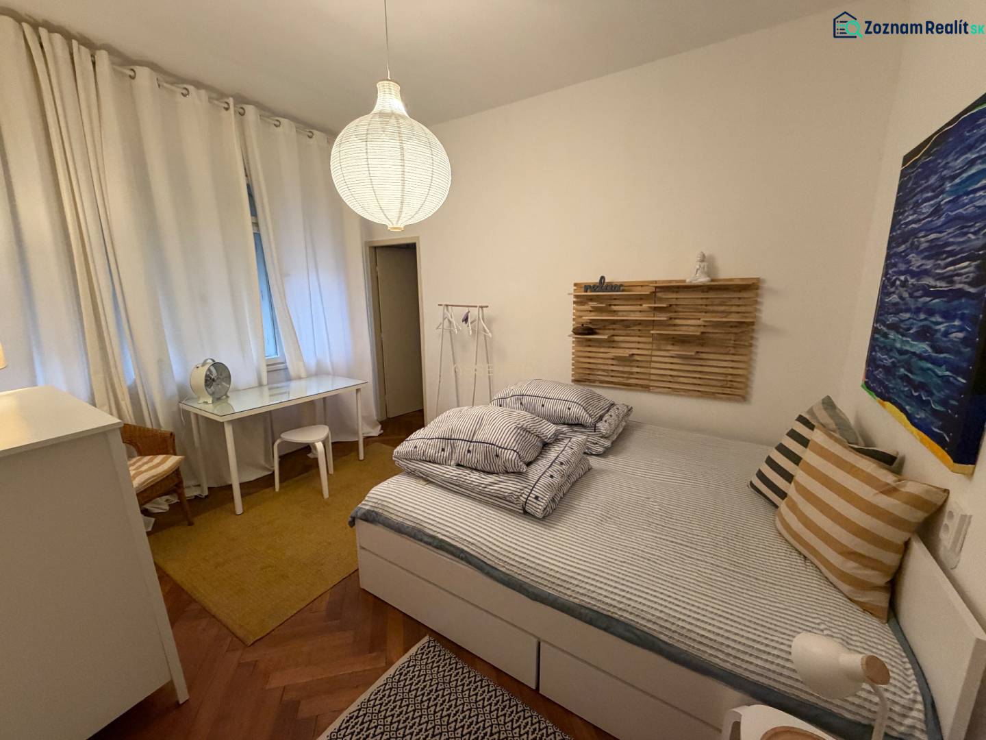 A bedroom in a two-room apartment with a wooden decor floor and minimalist furnishings.