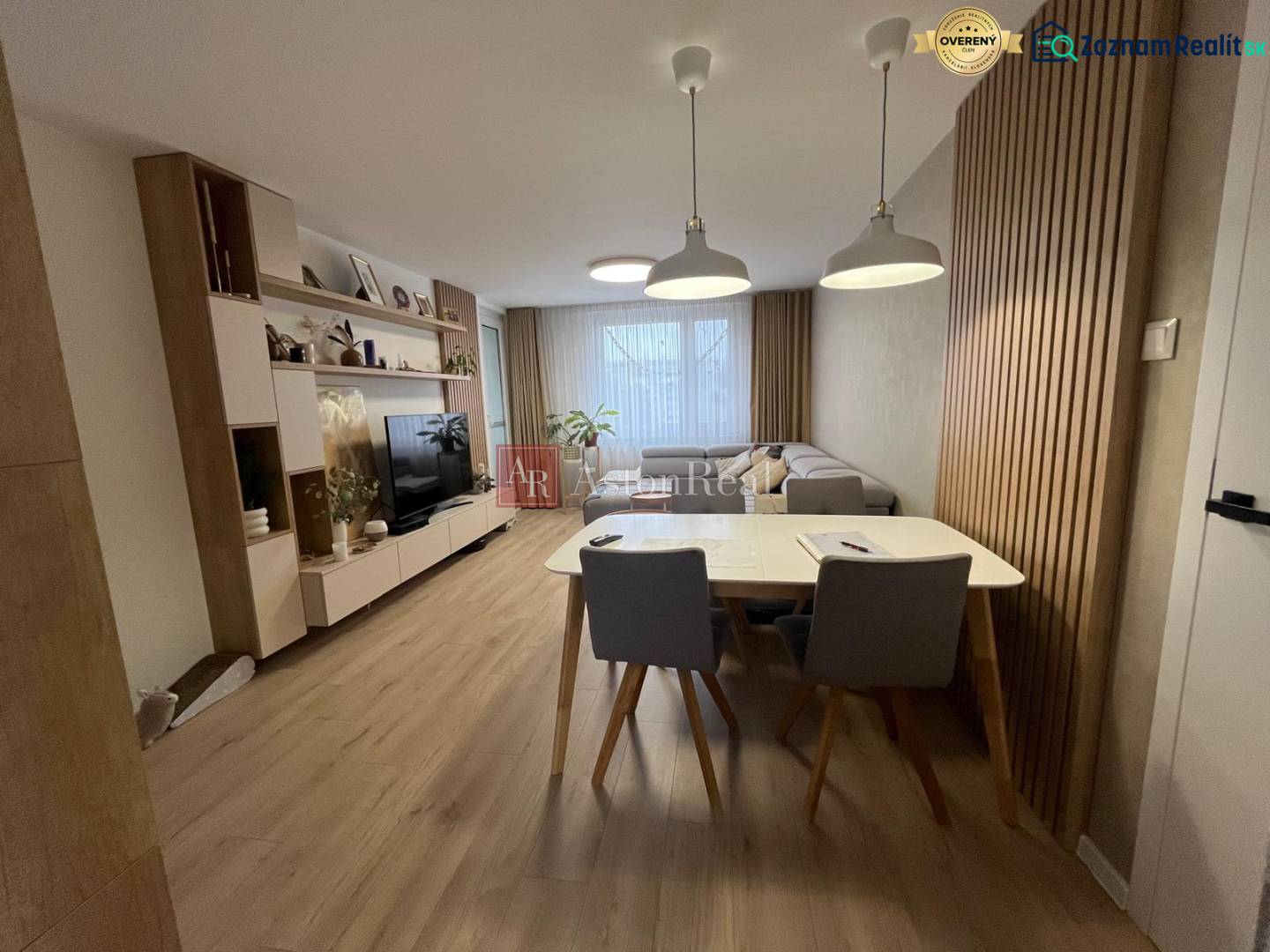 Living room in a 4-room apartment with a sofa, TV, dining table, and wooden decor flooring.