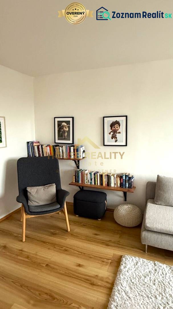 Living room with an armchair, a bookshelf full of books, pictures, and a floor with a wooden decor.