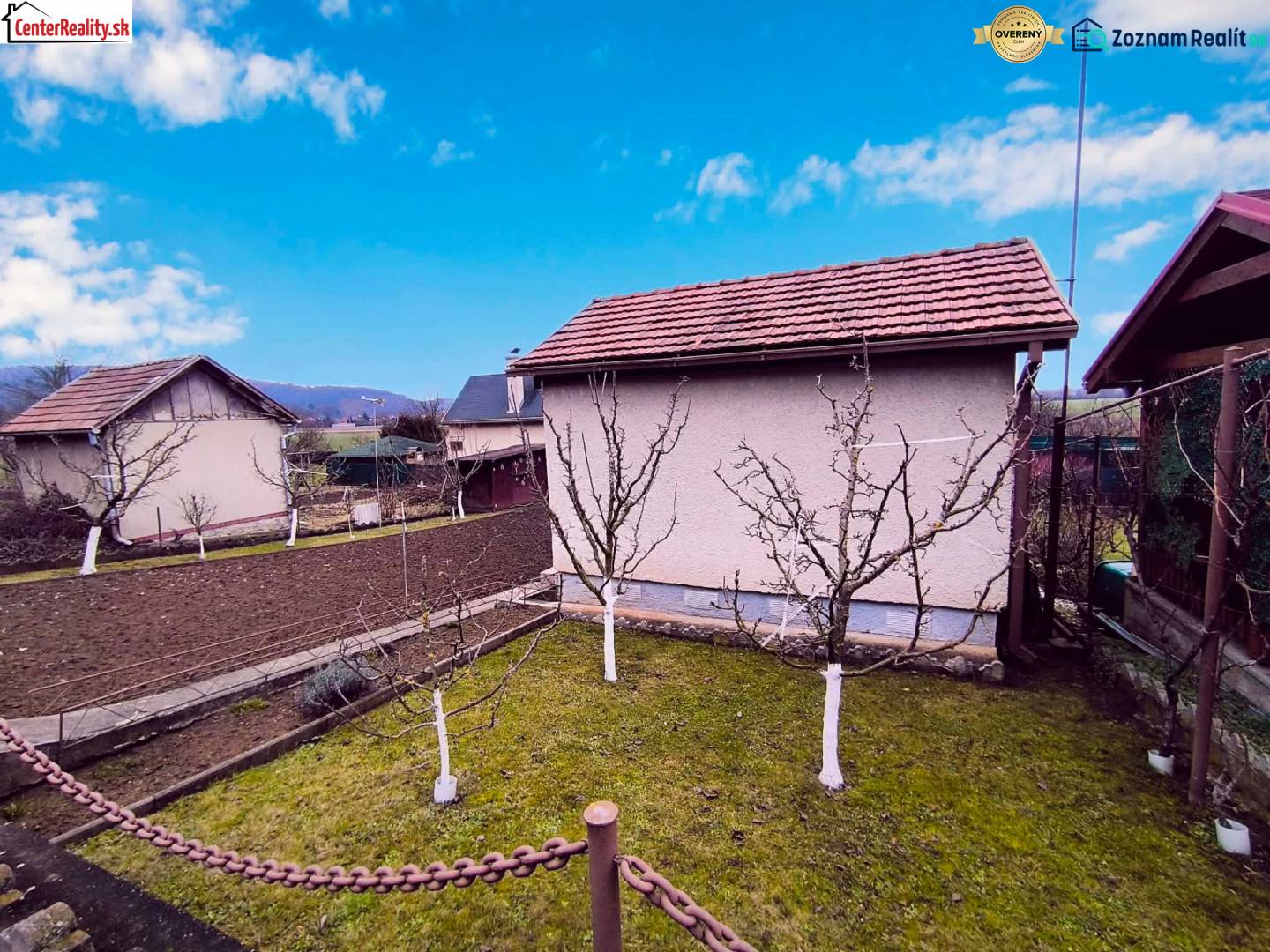 A garden with a cottage in Partizánske, fruit trees and cultivated land, clear sky.