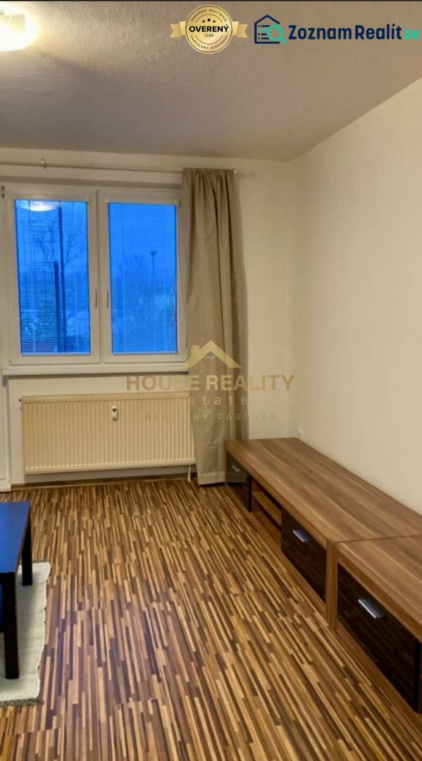 Living room in a three-room apartment with a wooden decor floor and a view through a large window.
