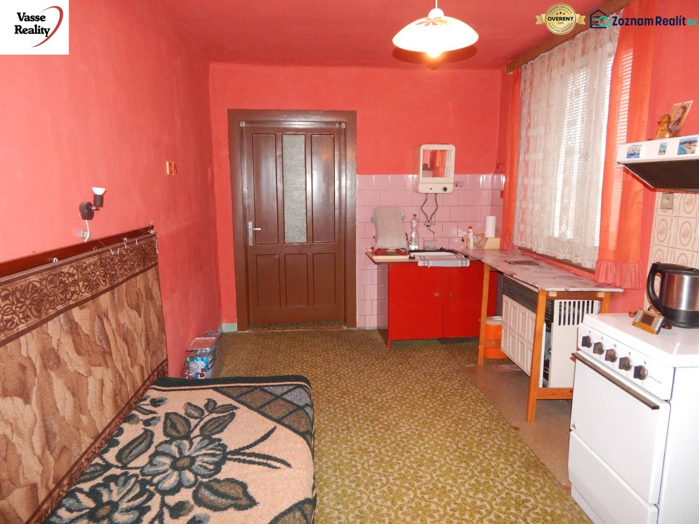 A kitchen in a family house with red walls, older furniture, and a green carpet.