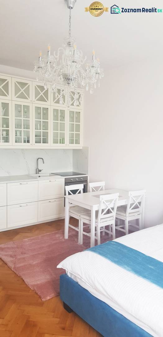 A kitchenette with white furniture, a table, and a crystal chandelier in a studio apartment.
