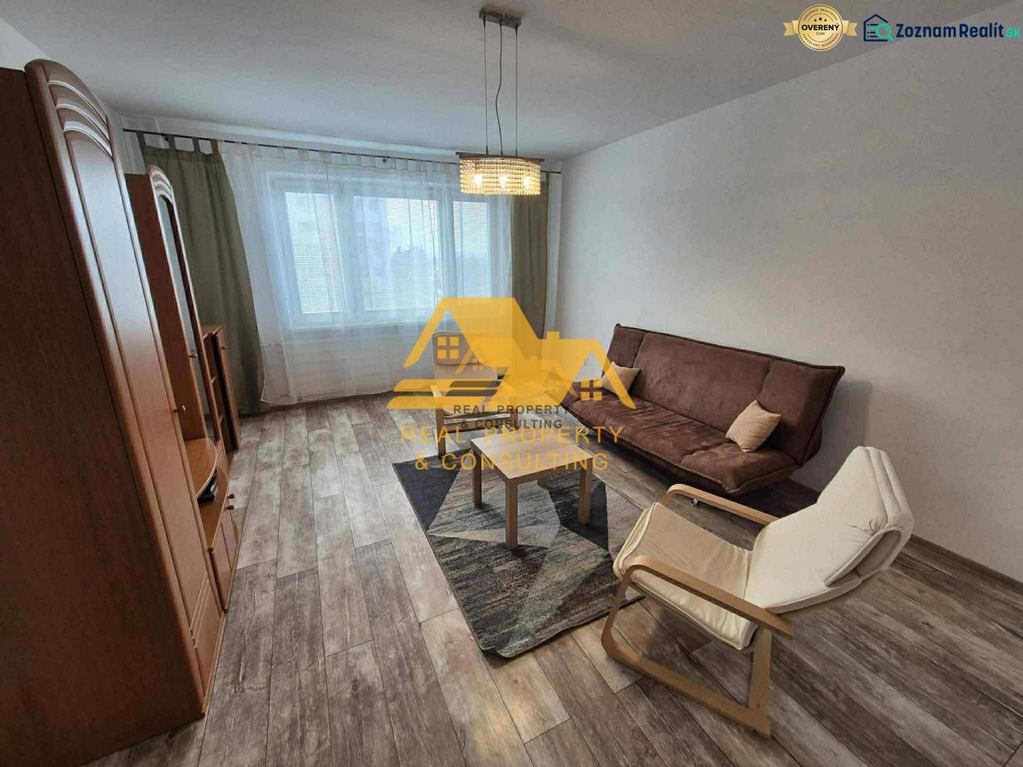 Living room in a 3-room apartment with a sofa, an armchair, and a wooden-patterned floor.