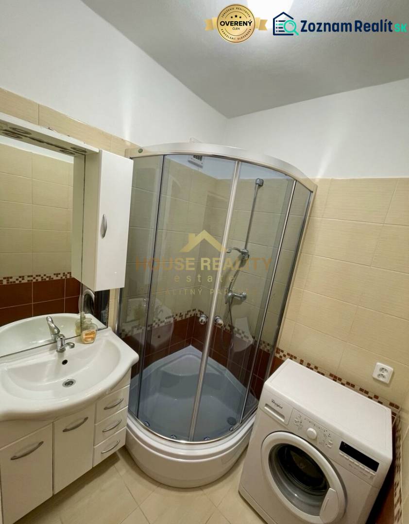 A bathroom in a one-room apartment with a bathtub, washing machine, and sink.