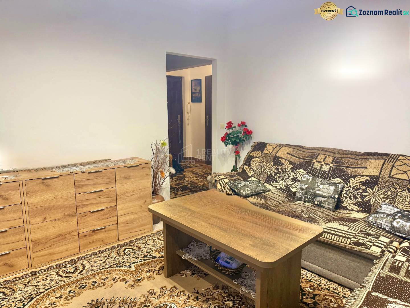 Living room in a two-room apartment with a wooden sideboard and a patterned carpet.