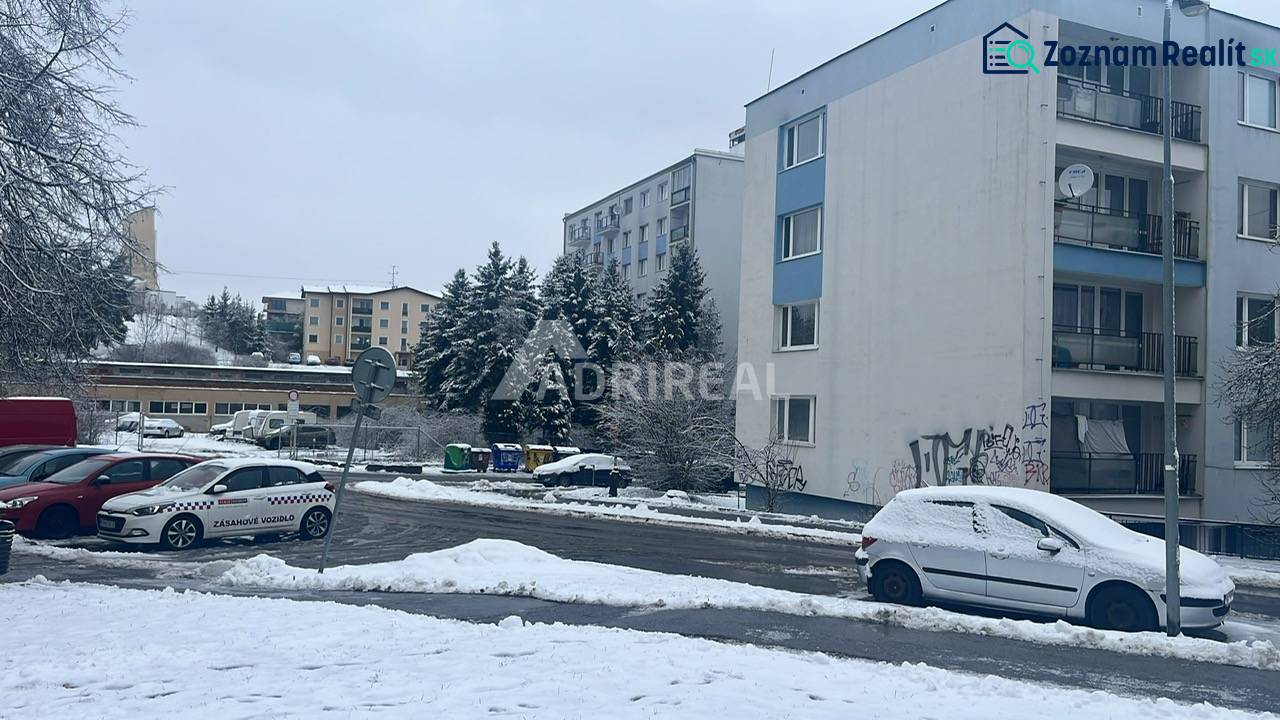 A snowy Bazovského street in Zvolen with parked cars next to a multi-story building.