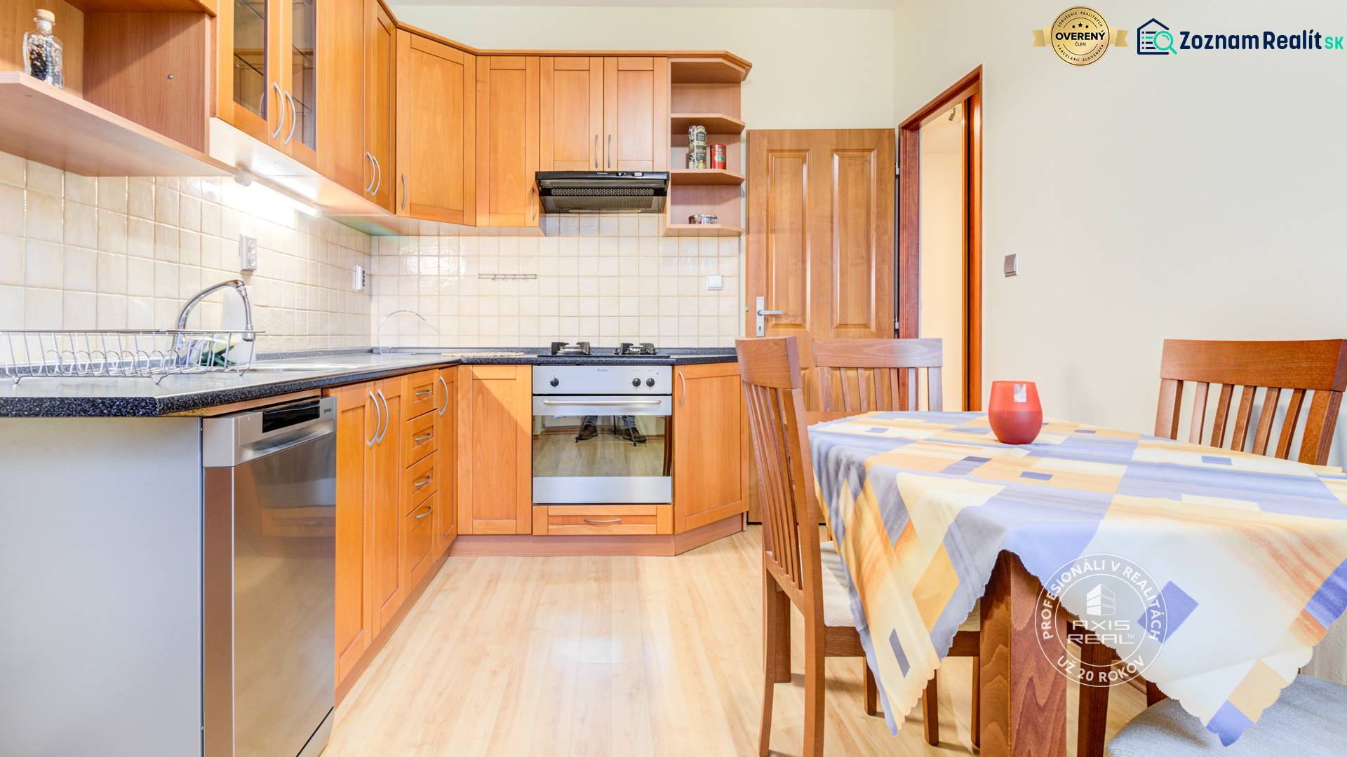 The kitchen of a two-room apartment with a kitchen unit, table, and wooden decor flooring.
