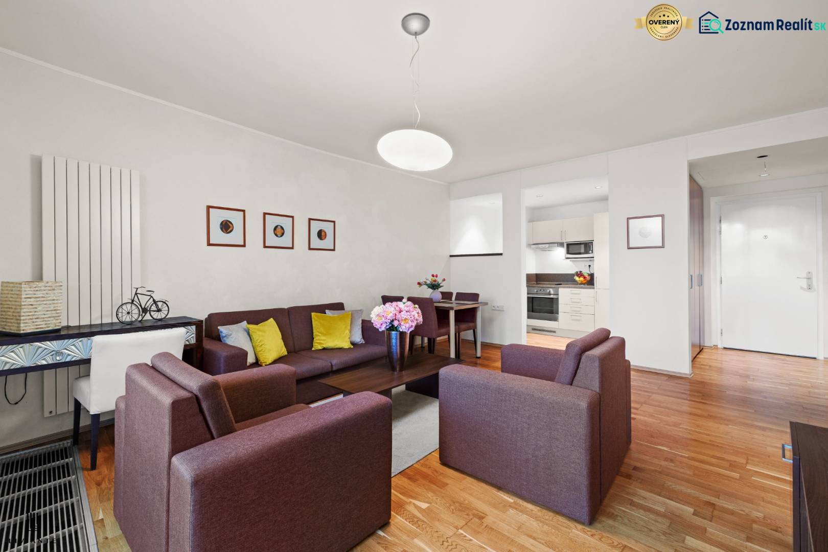 Living room in a two-room apartment with a wood-patterned floor, comfortable sofas, and a kitchenette.