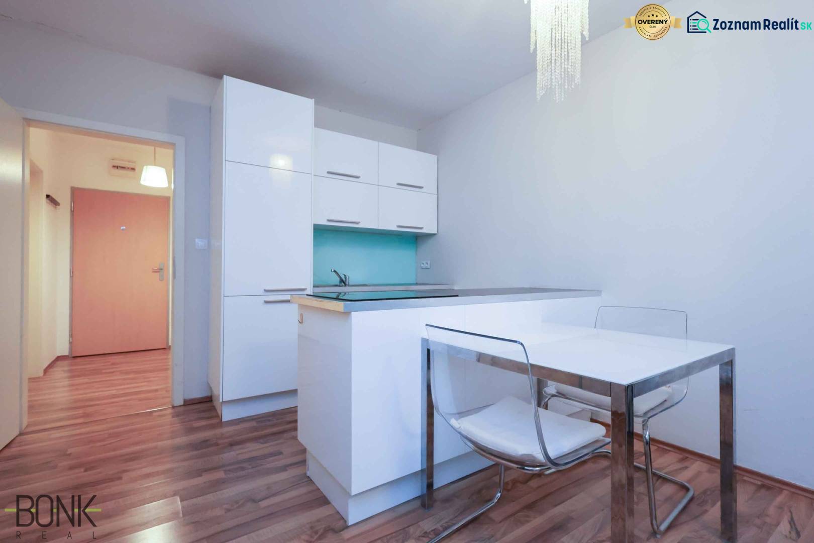 A kitchen in a 2-room apartment with white cabinets and a wooden decor floor.