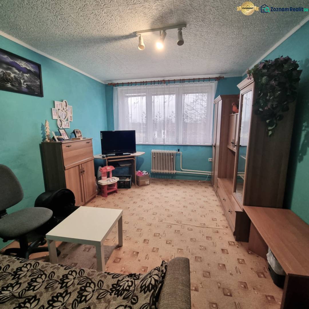 Living room in a three-room apartment with turquoise walls, furniture, and carpet flooring.