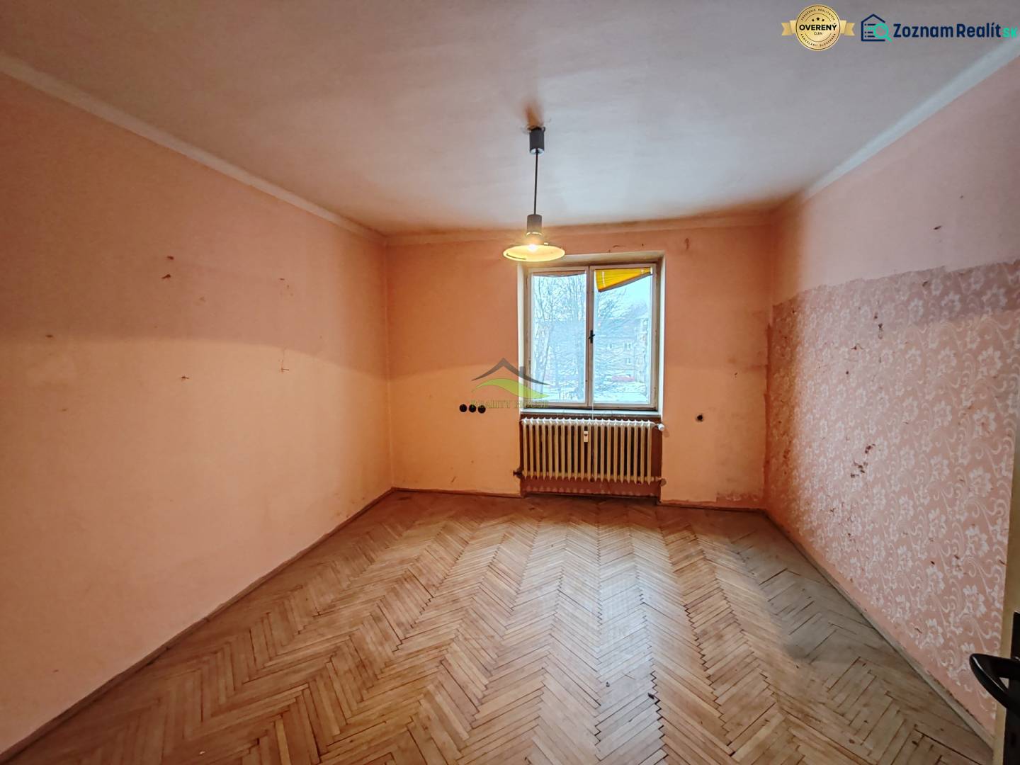 A room in a 2-room apartment with a wooden decor floor and a window with a radiator.