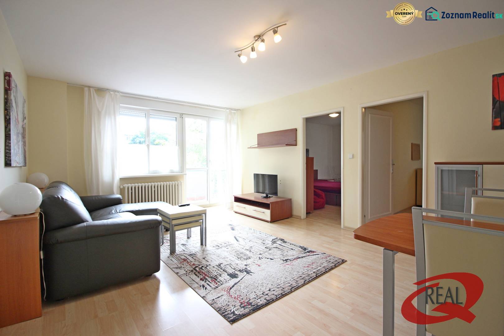 Living room of a three-room apartment with a sofa, table, and television on a wooden-decor floor.