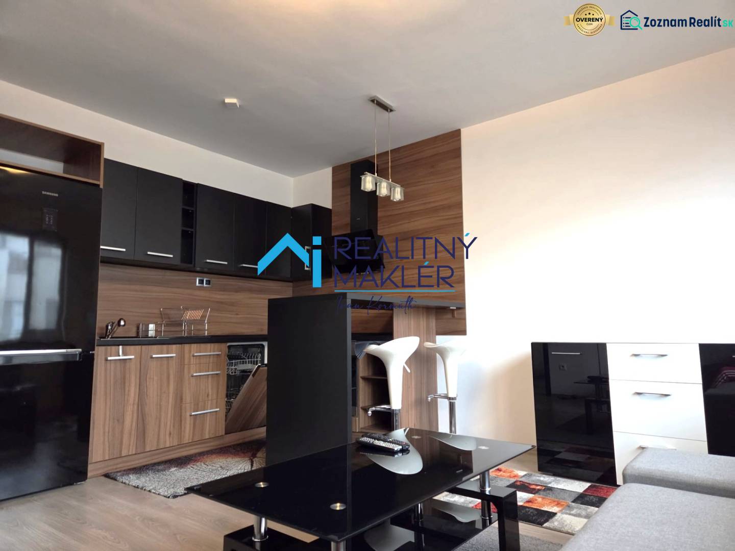 A kitchen in a studio apartment with black cabinets, flooring with a wood decor.