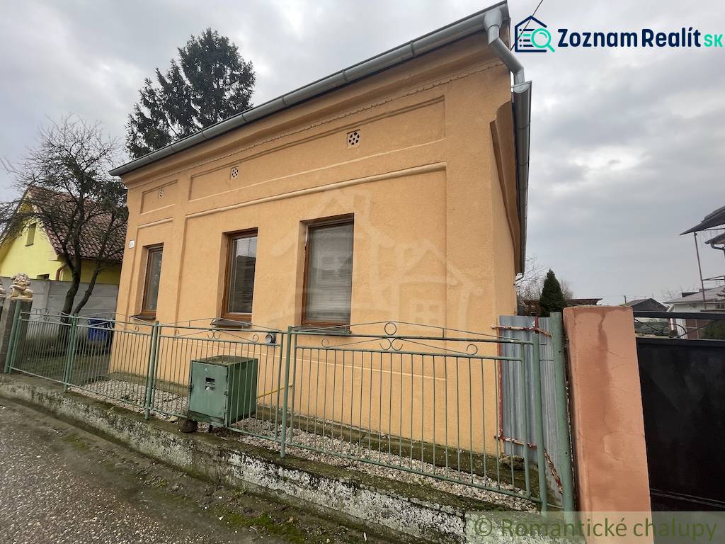 An orange family house in Neded surrounded by a fence, next to trees and other houses.