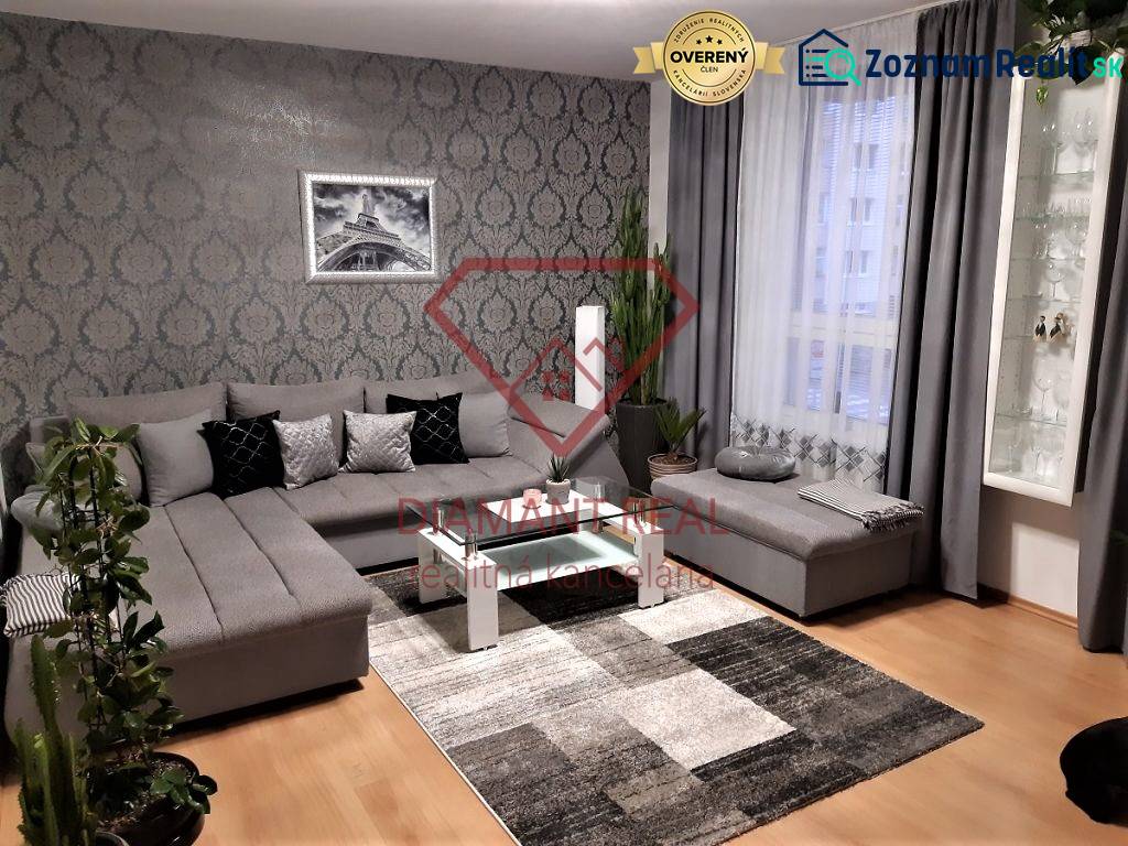 Living room with a large gray sofa, decorative wallpaper, and wood-patterned flooring.