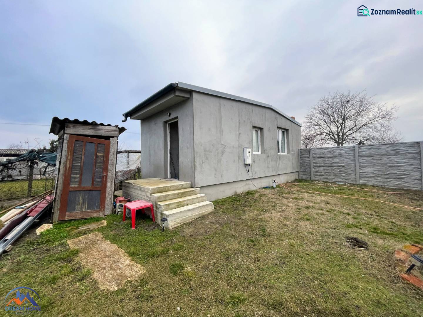 A house in Komárno with a concrete facade, a staircase, and a garden surrounded by a fence.