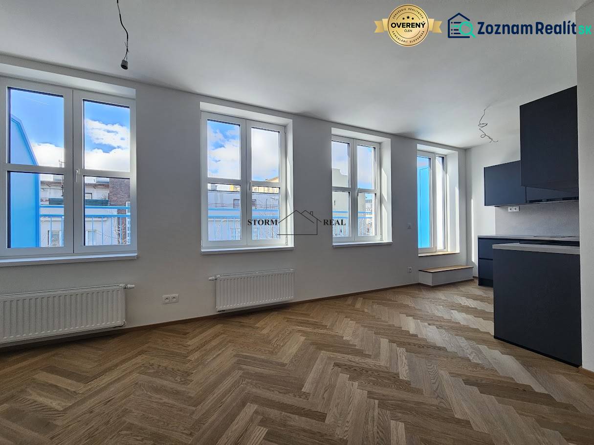 A one-bedroom apartment with a wooden decor floor and a black kitchen unit.