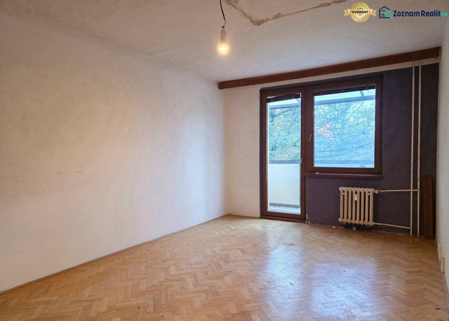 A vacant room in a 2-room apartment with a wooden decor floor and a window to the balcony.