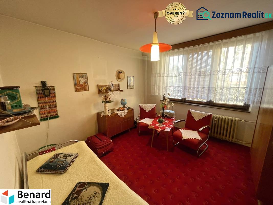 A room in a 3-room apartment with older furniture, a red carpet, and decorations.