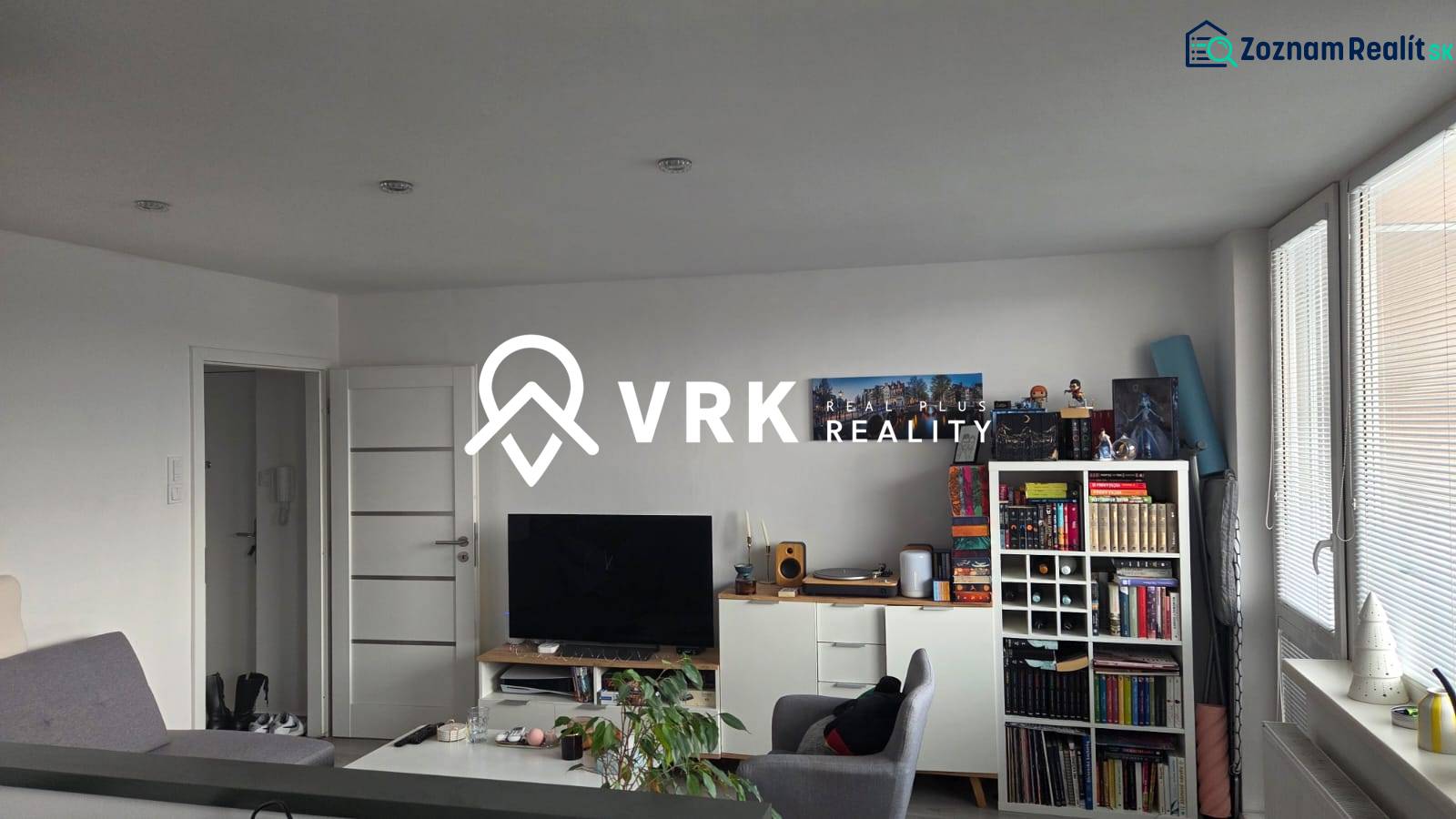 Living room of a three-room apartment with a bookshelf, television, and light-colored furniture.