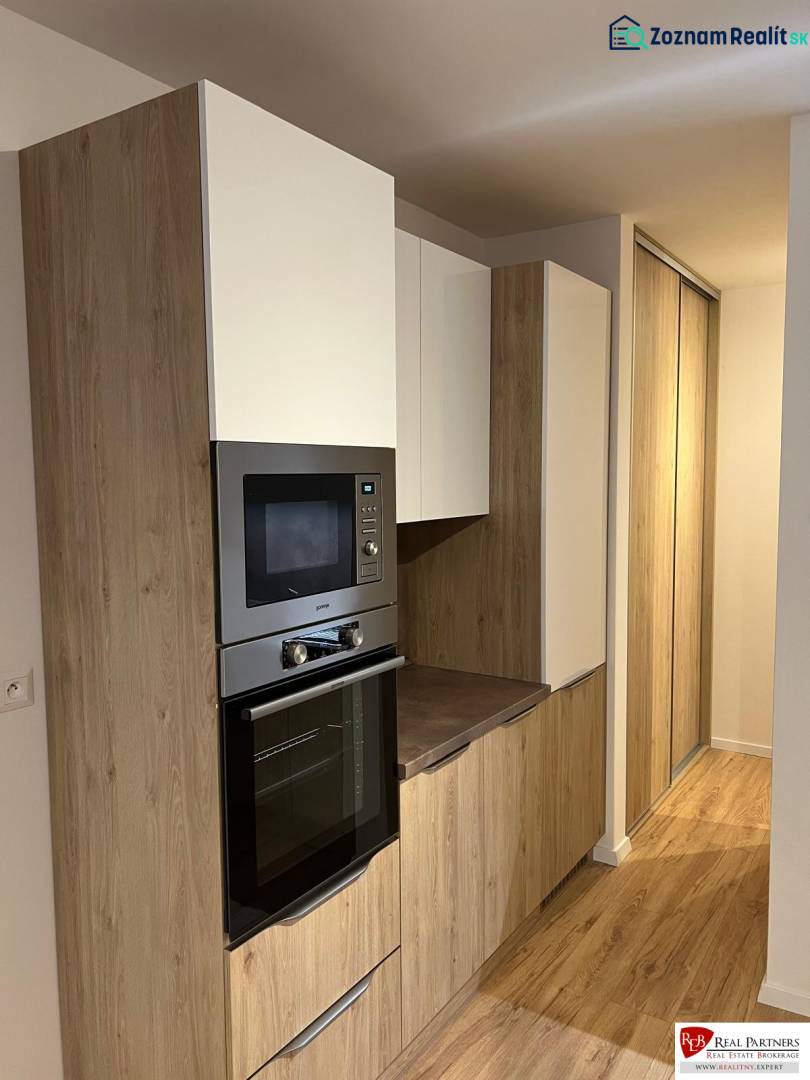 Kitchen area of a two-room apartment with a wooden decor floor and built-in cabinets.