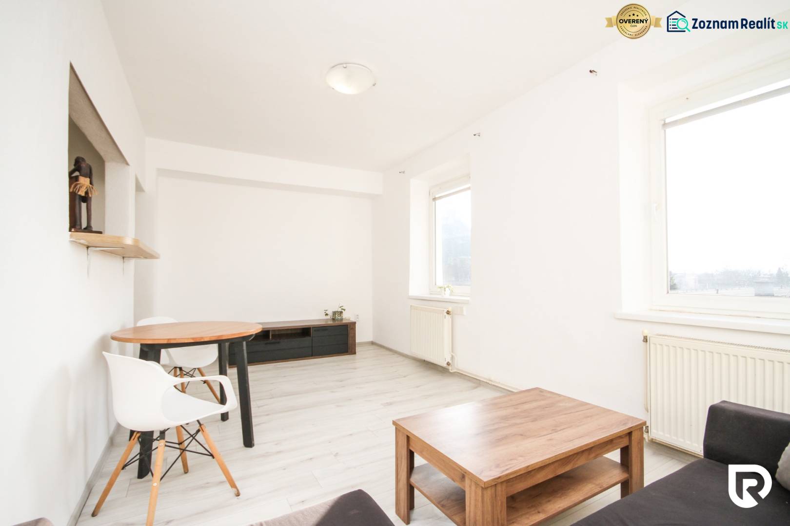 A bright living room in a two-room apartment with a wooden decor floor and simple furniture.