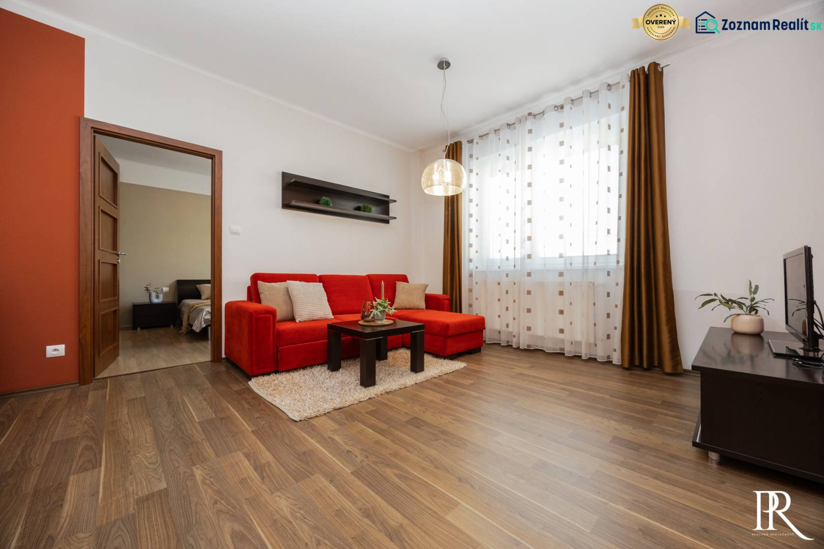 Living room in a two-room apartment with a red sofa and wood-patterned flooring.