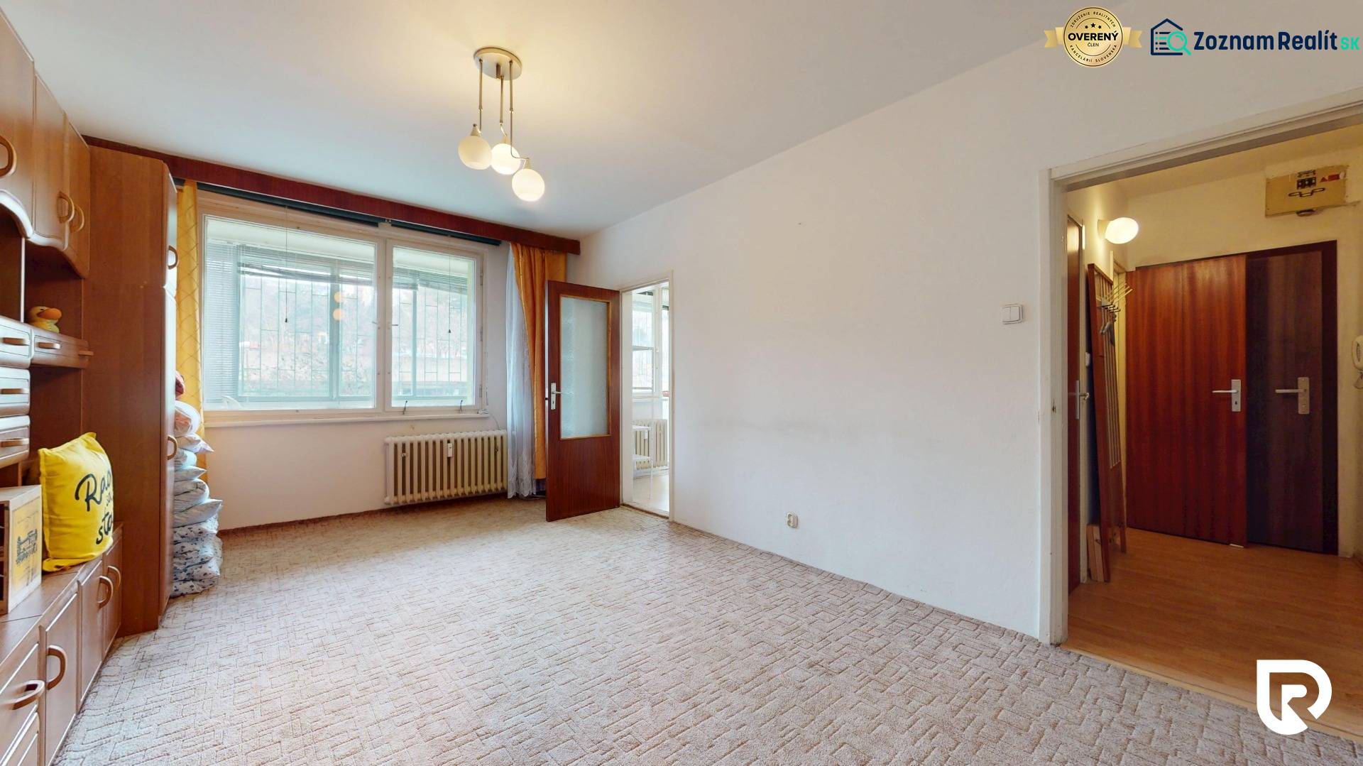 Living room in a two-room apartment with a carpet, radiator, and wall cabinets.