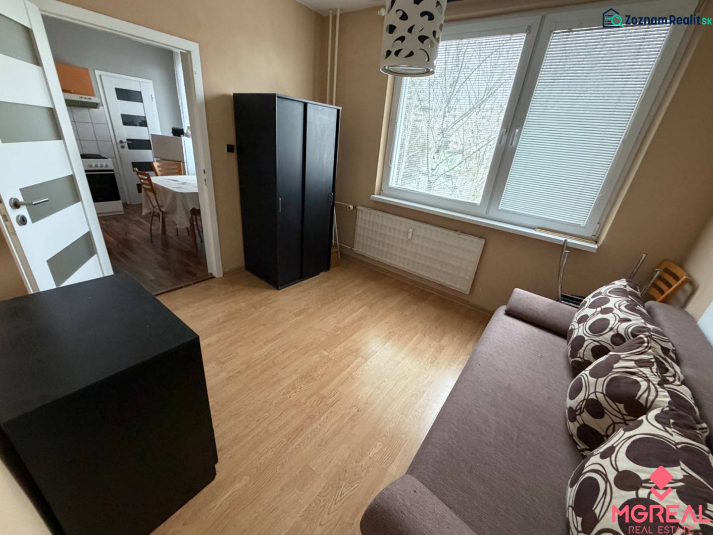 A room in a 3-room apartment with a wooden decor floor and simple furniture.